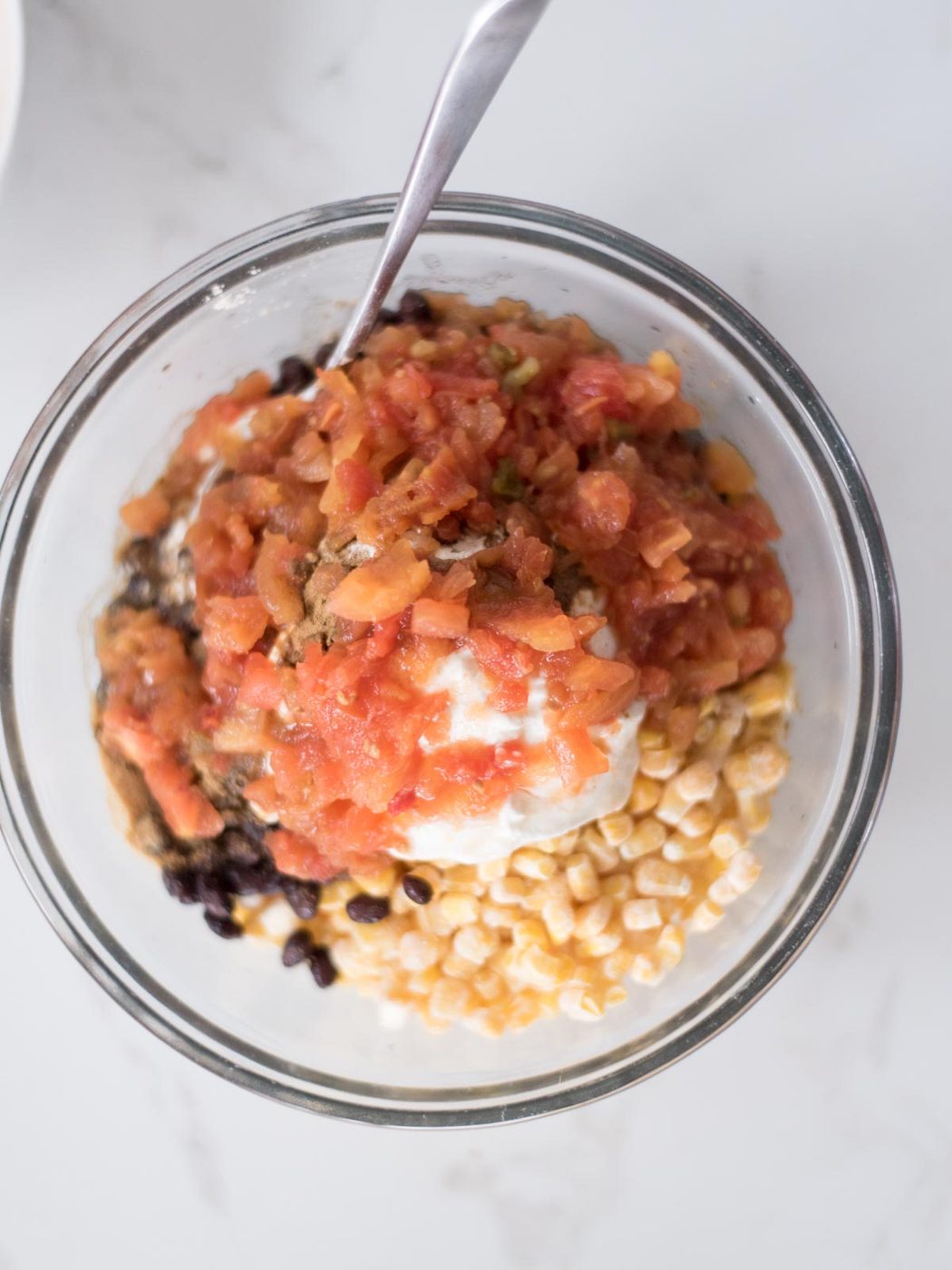 Tomatoes topping the corn and sour cream mixture in a mixing bowl.
