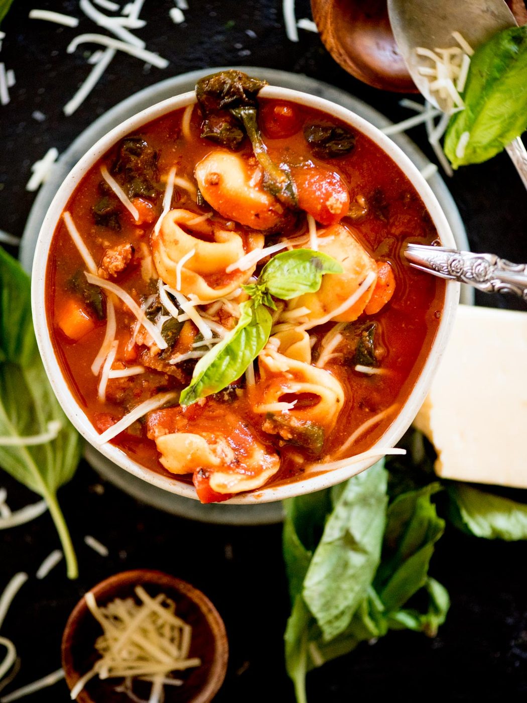 spinach tortellini soup in a bowl topped with grated parmesan and fresh basil