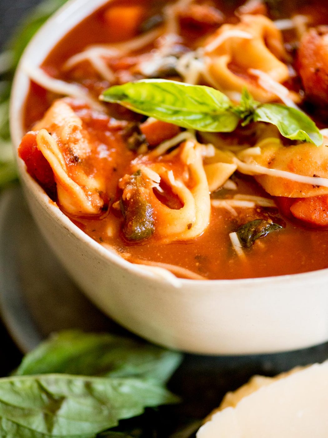 spinach tortellini soup topped with grated parmesan and fresh basil