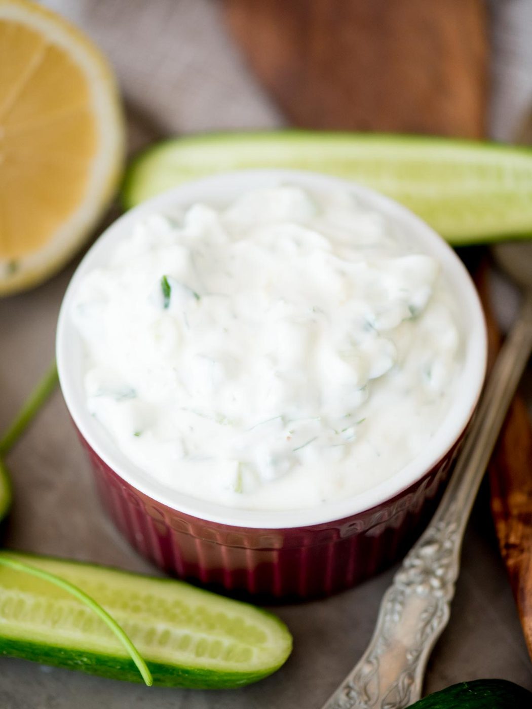 tzatziki sauce in a bowl surrounded by cucumbers and lemons