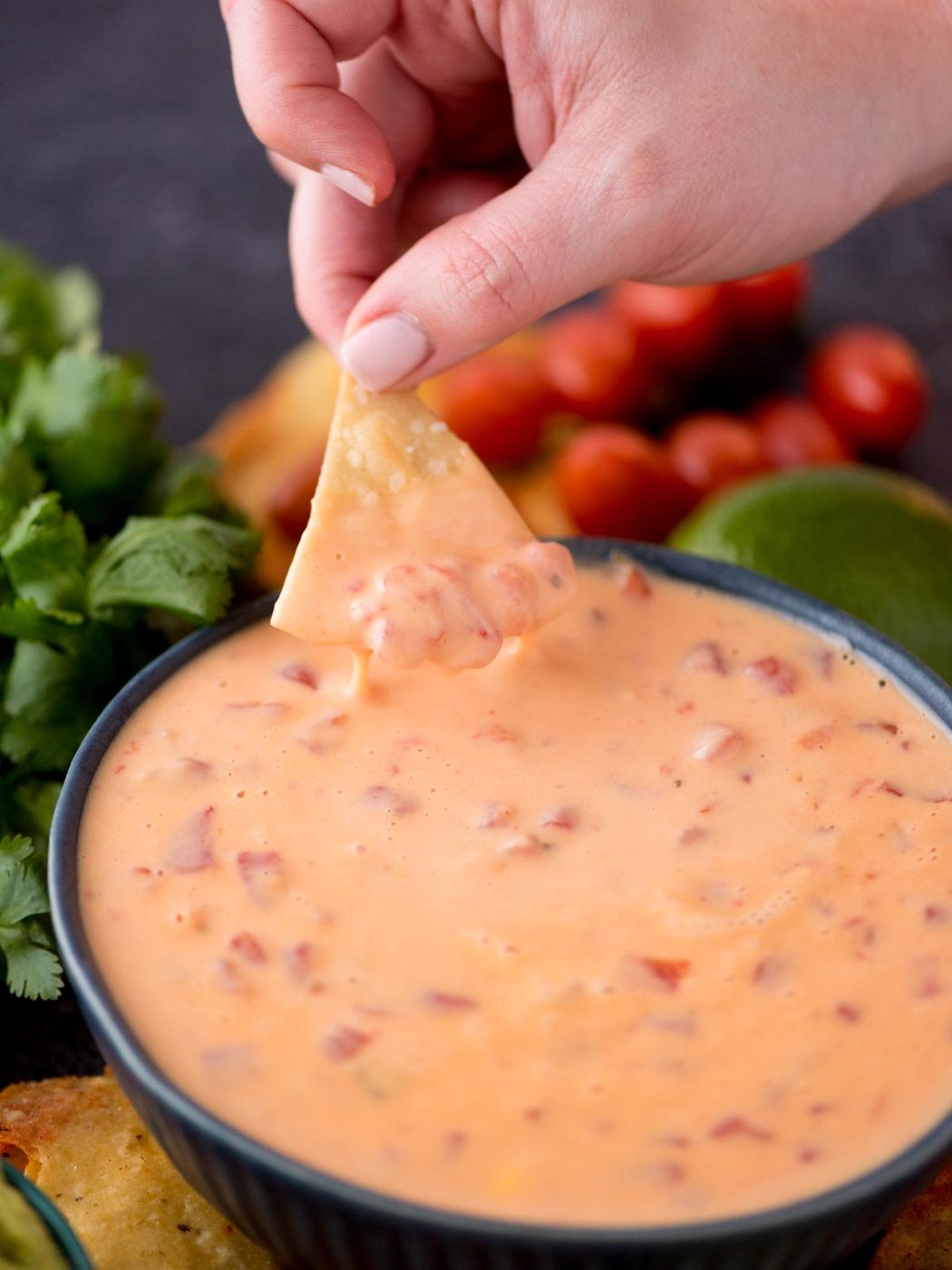 Hand dipping a tortilla chip into a bowl of velveeta queso.