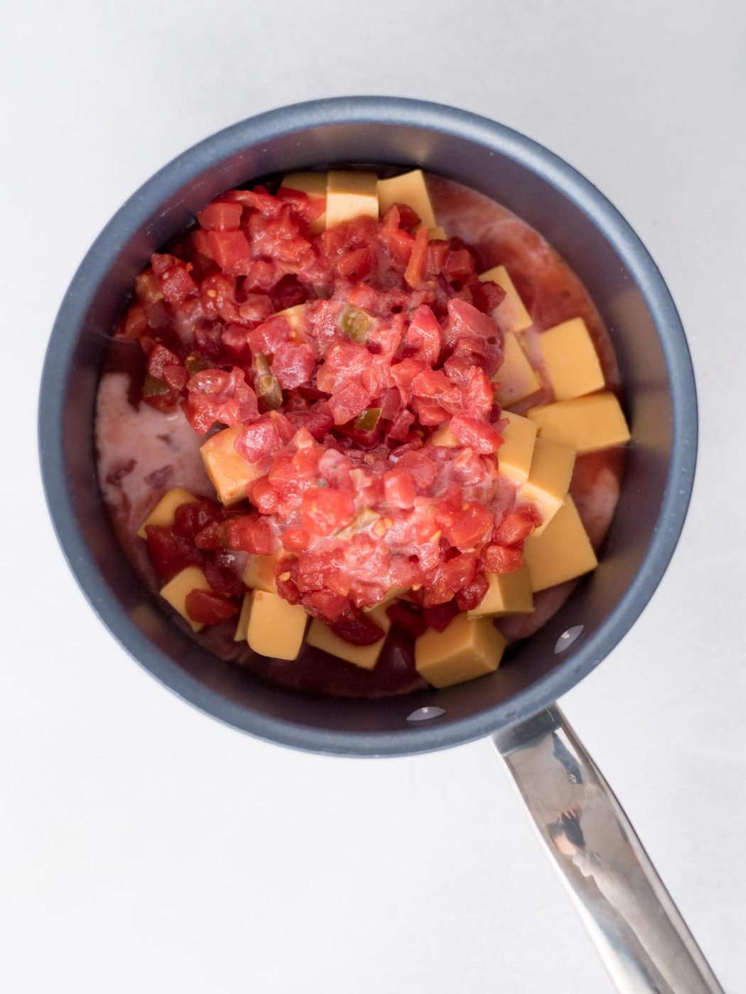 Saucepan with velveeta cheese, diced tomatoes and milk added to the ingredients.