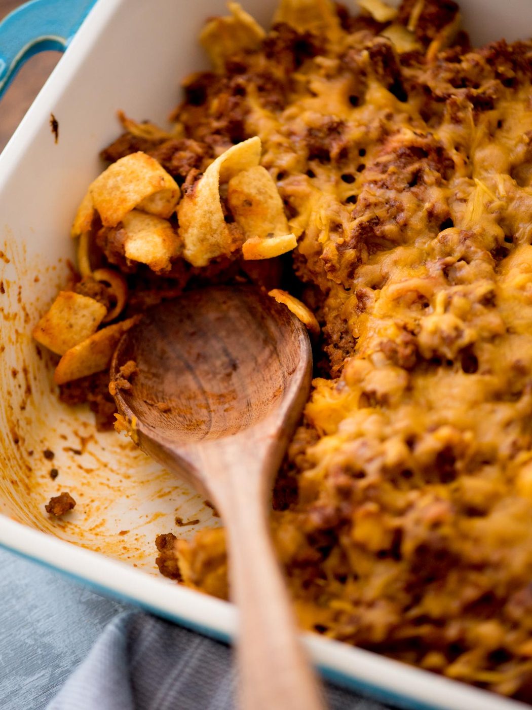 A wooden spoon sitting in a casserole dish with a serving gone of walking taco casserole.