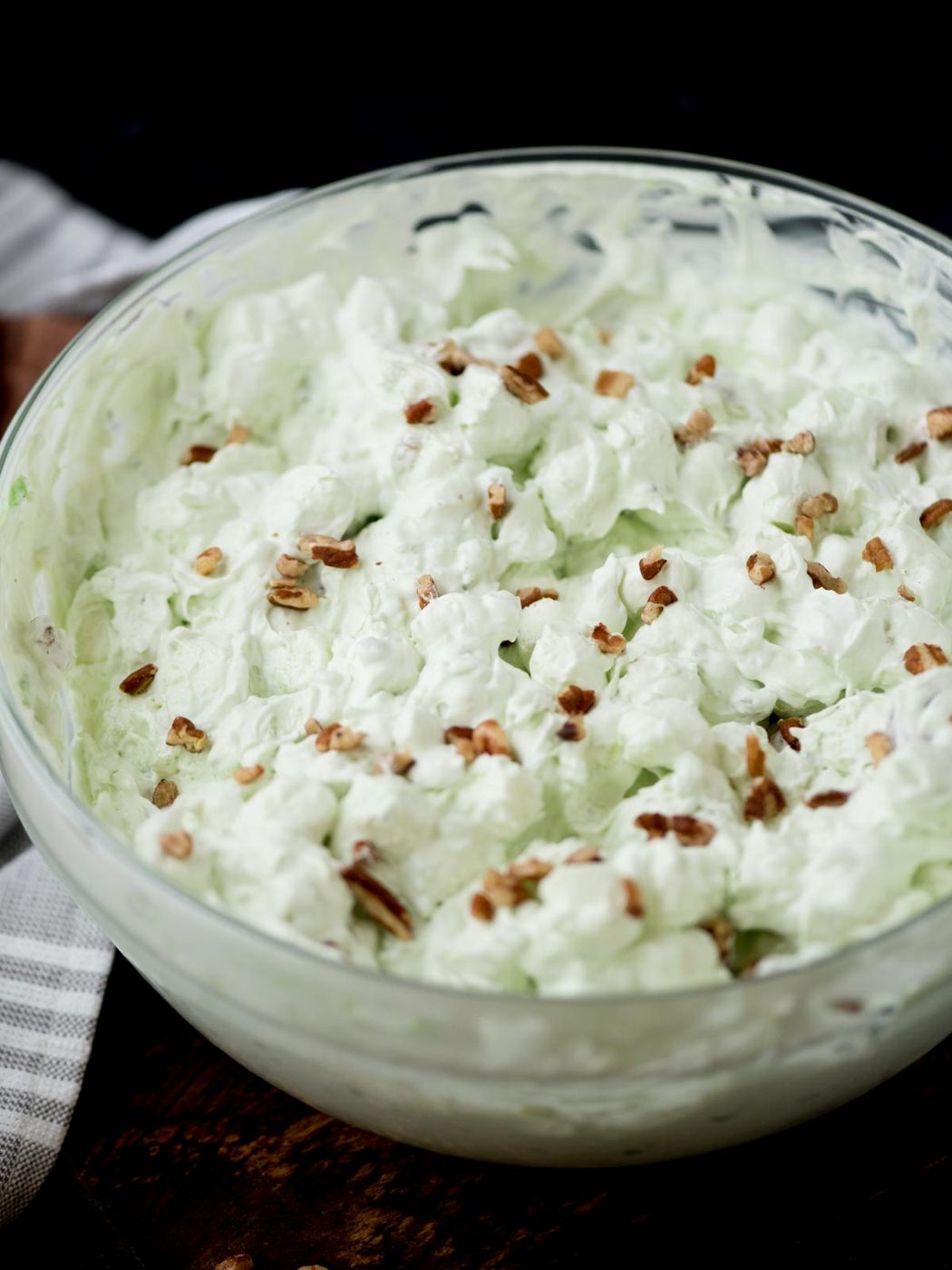 pistachio salad in a glass bowl surrounded by a kitchen towel and serving utensils