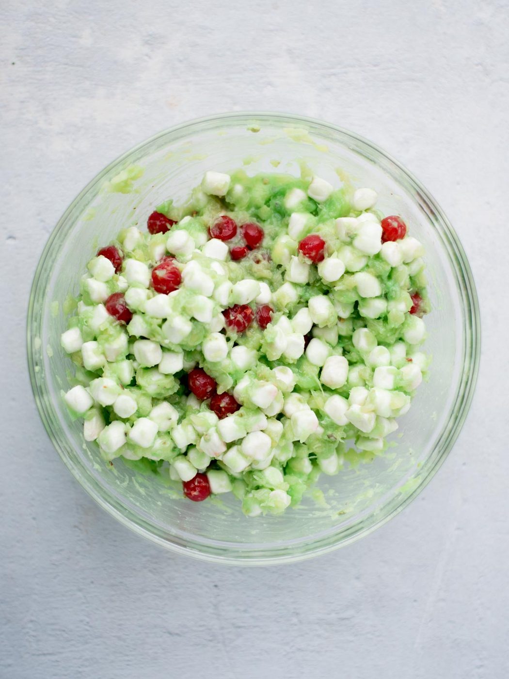 pistachio pudding mix, pineapple, marshmallows, and cherries mixed together in a bowl
