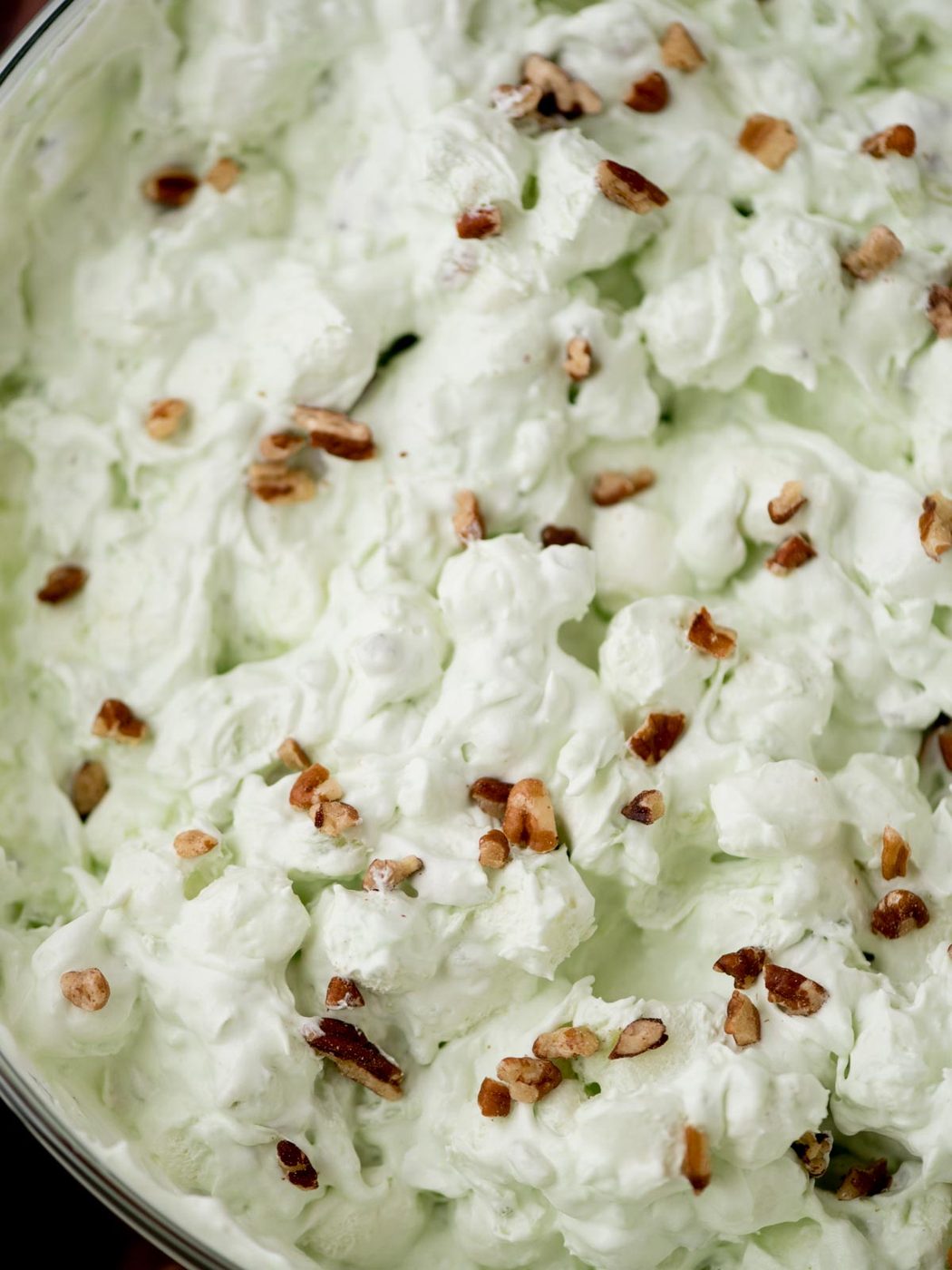 pistachio salad in a glass bowl surrounded by a kitchen towel and serving utensils