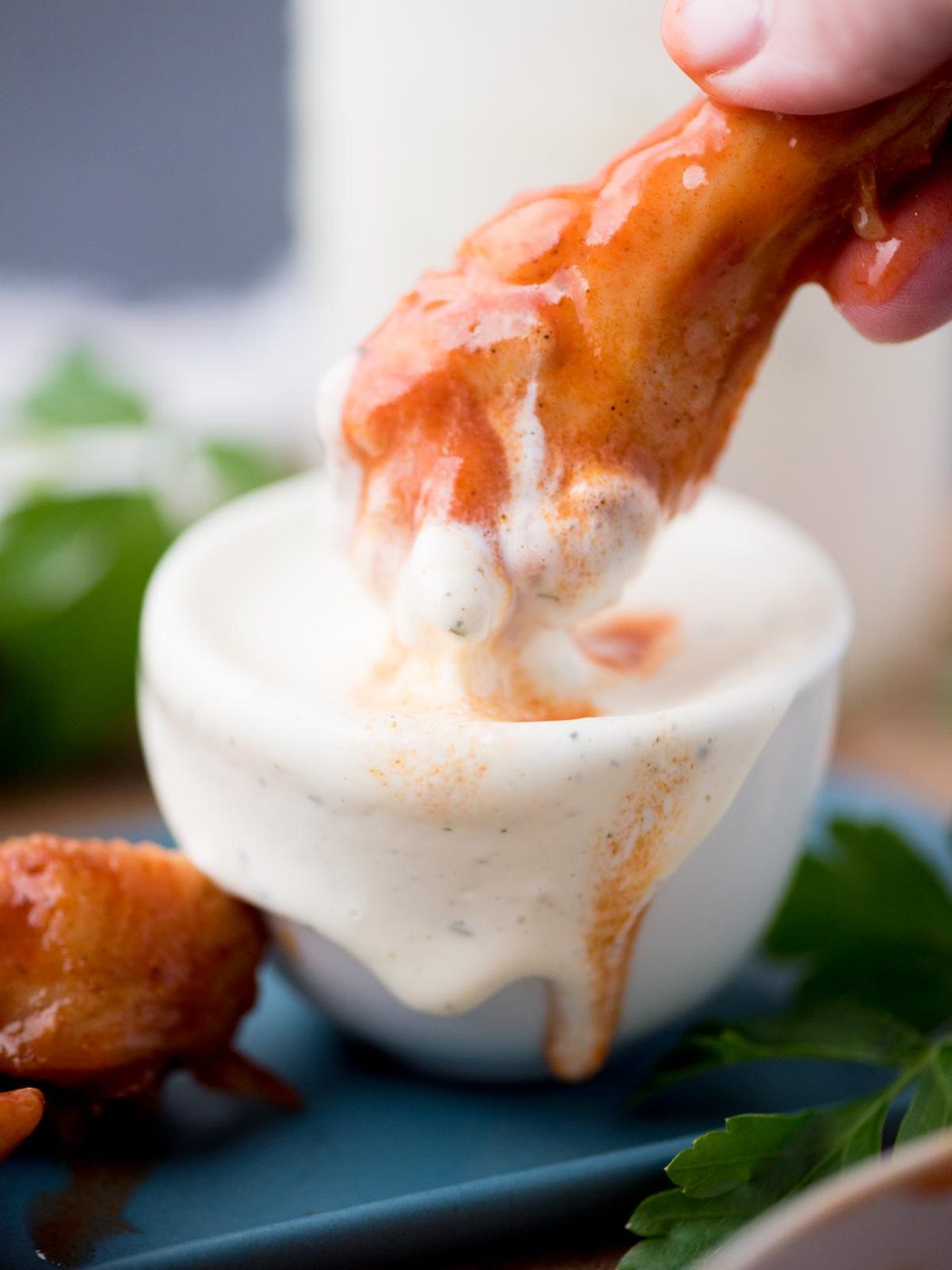 Hand dunking a drumstick in a small bowl of wingstop ranch.