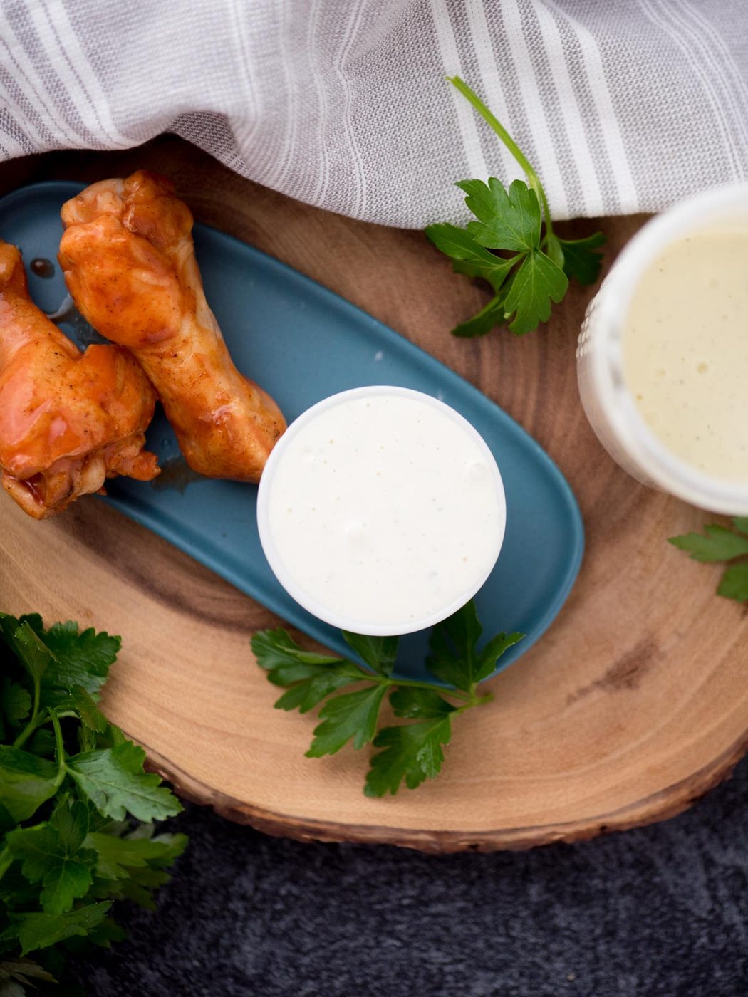 Drumsticks on a plate next to a small bowl of wing stopranch and cilantro leaves garnished on the side.