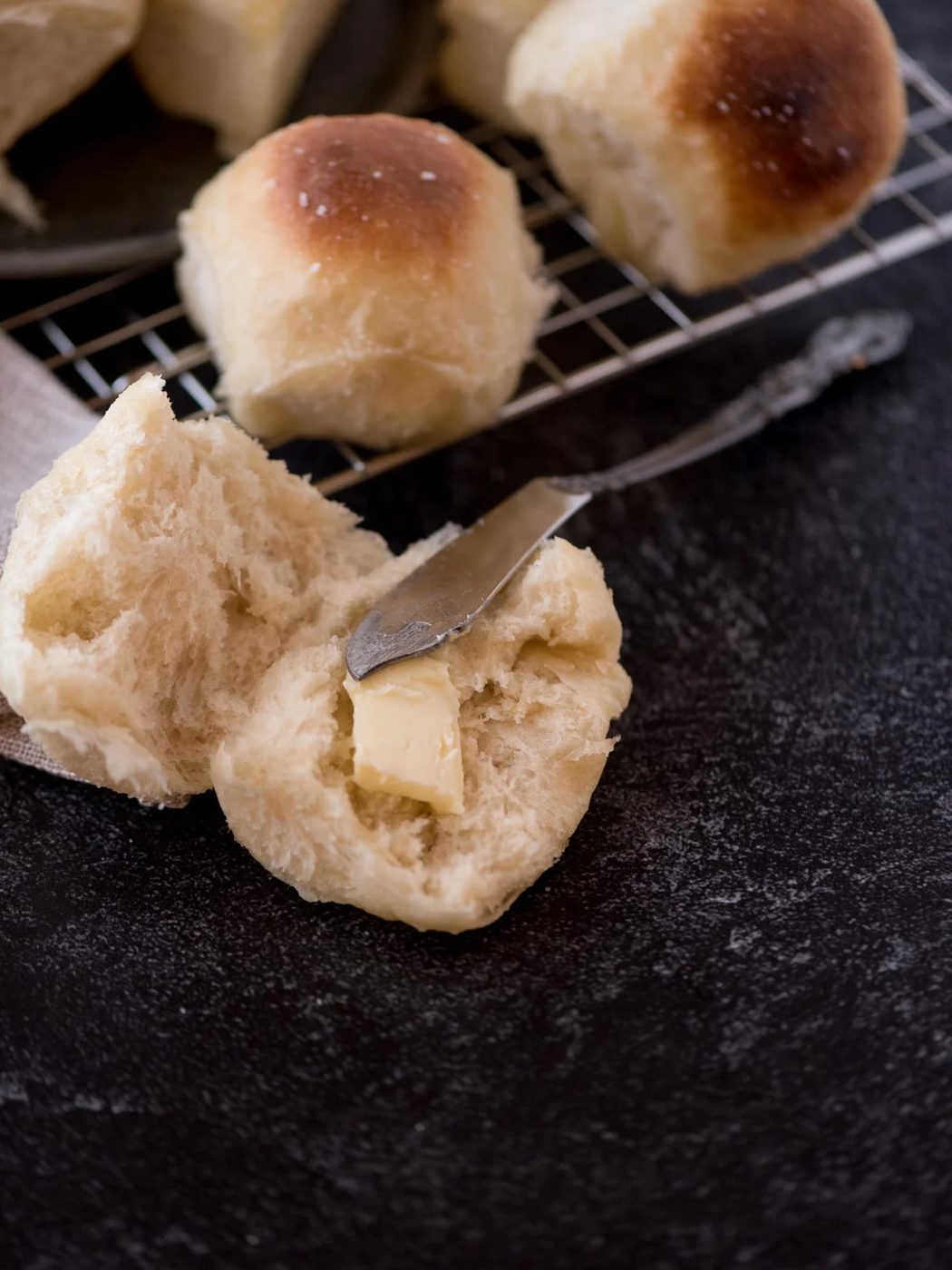 a yeast roll that has been cut open with butter on it and the knife resting in it