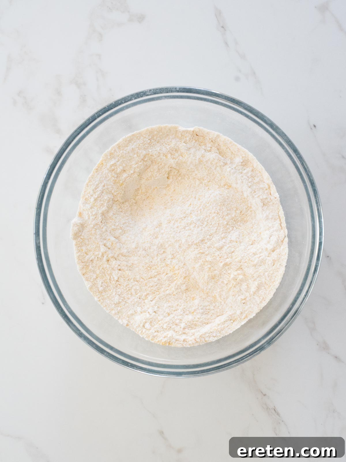 Dry ingredients like flour, cornmeal, sugar, baking powder, and salt are mixed together in a bowl
