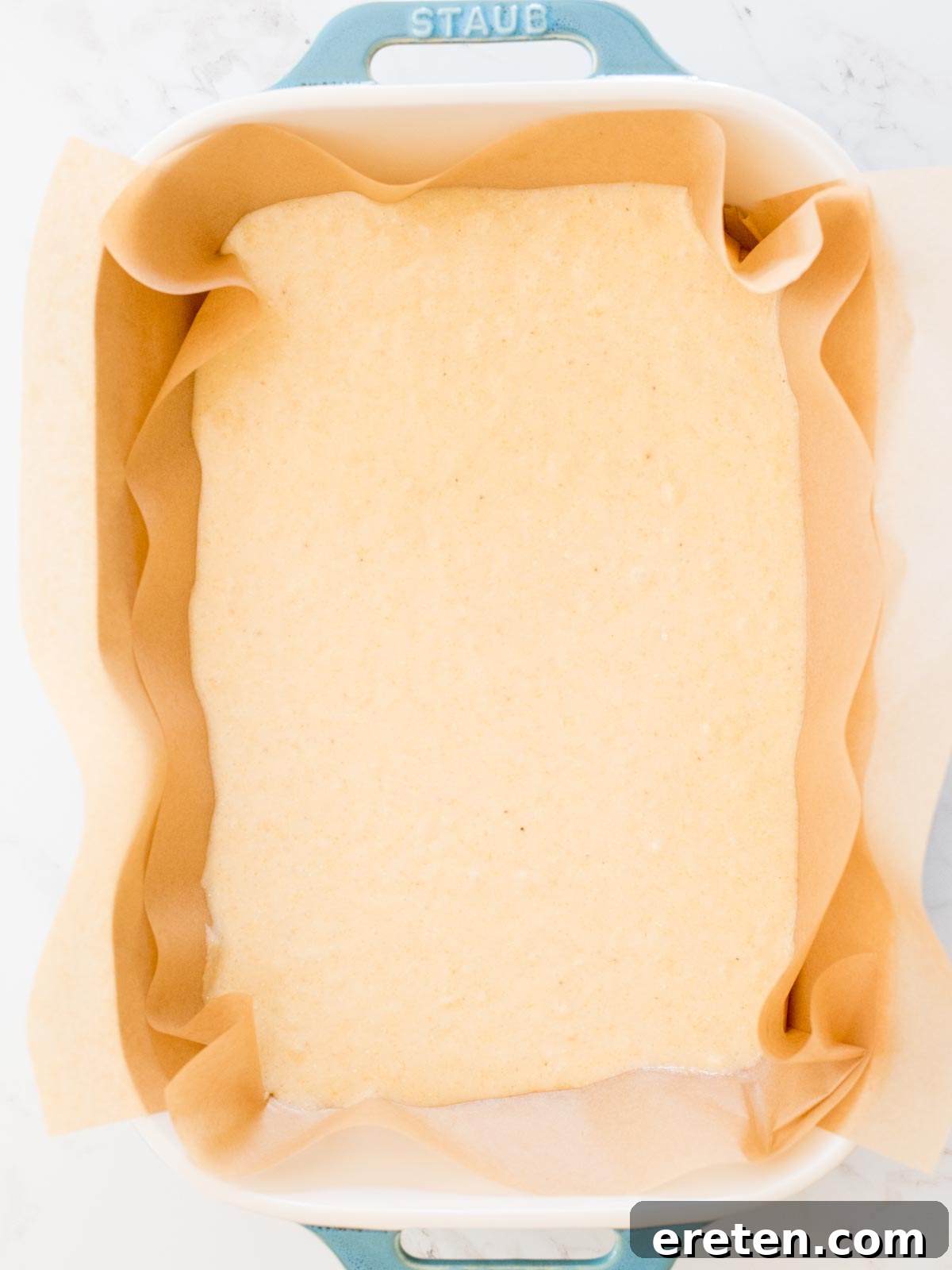 Unbaked cornbread batter uniformly spread in a parchment-lined baking dish