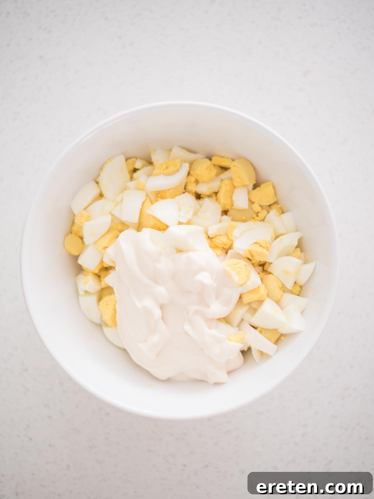 Dill-icious Egg Salad: Perfect for Quick Wraps and Elegant Tea Sandwiches 5 Mayonnaise being added to chopped eggs in a mixing bowl for a creamy egg salad recipe