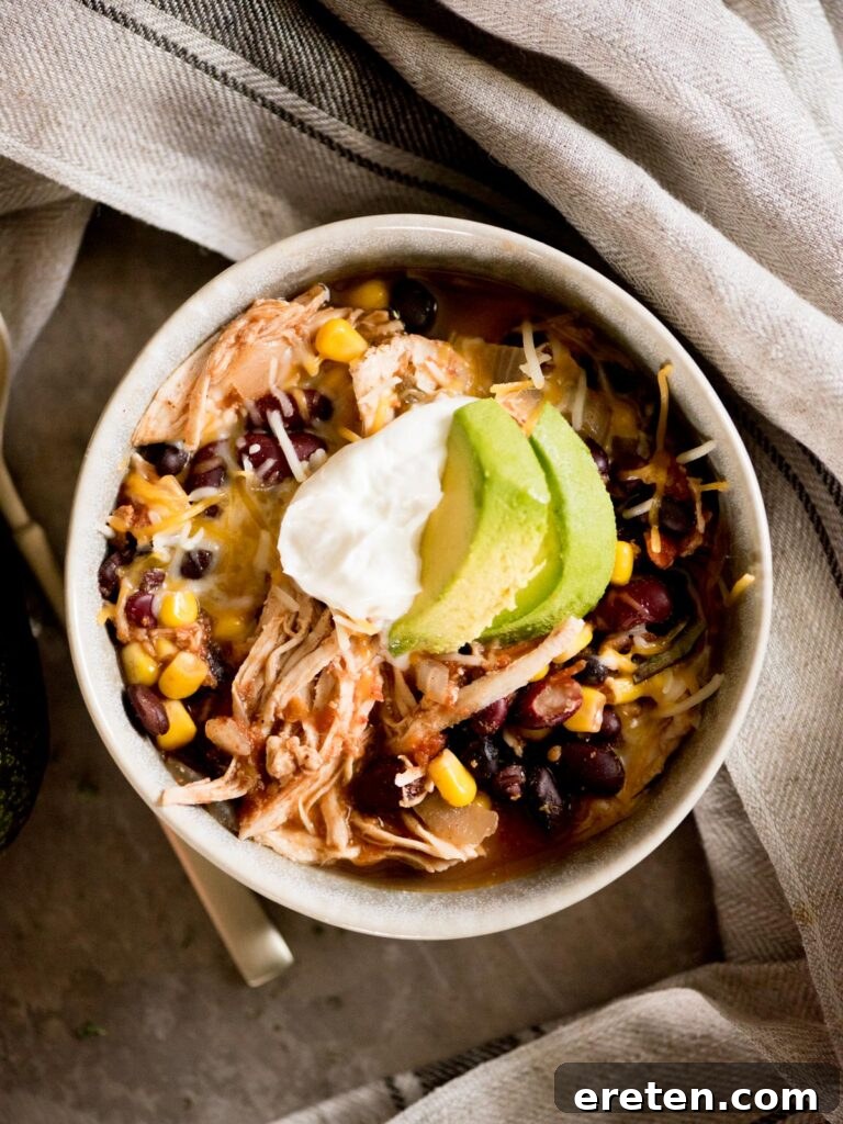 A bowl of vibrant Mexican chicken chili, generously topped with cool sour cream and fresh avocado slices, ready to be enjoyed.
