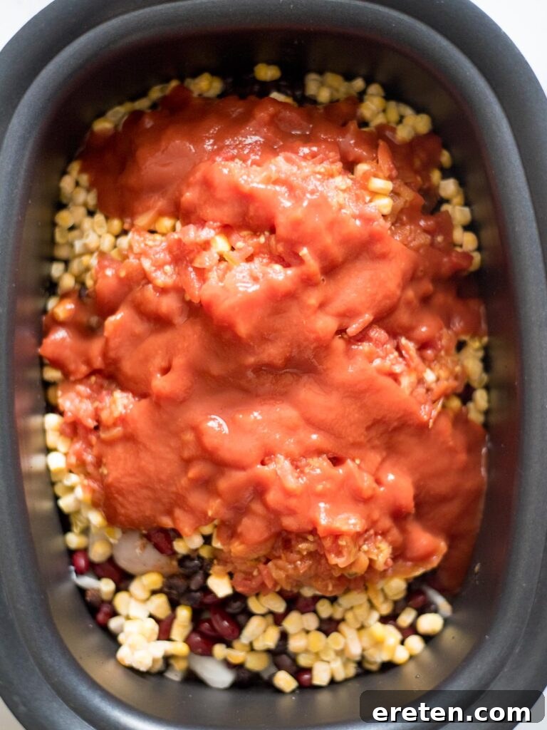 Tomato sauce is poured over all the ingredients in the slow cooker, ensuring a rich, cohesive chili consistency.