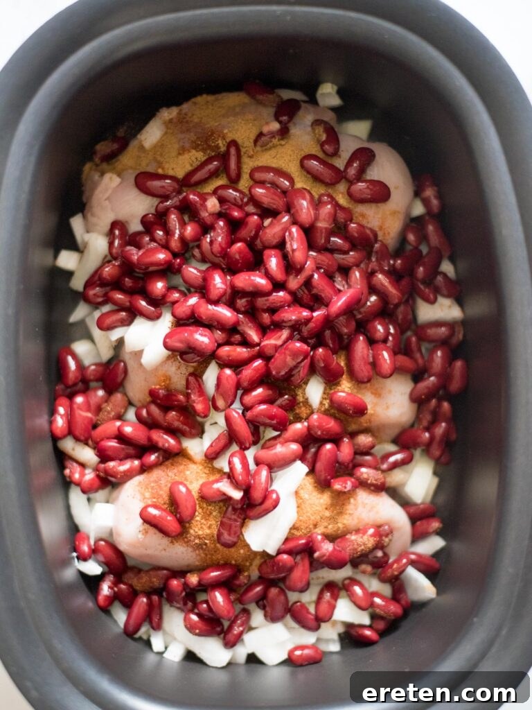 A layer of kidney beans is added to the slow cooker, complementing the chicken and onions for the chili base.