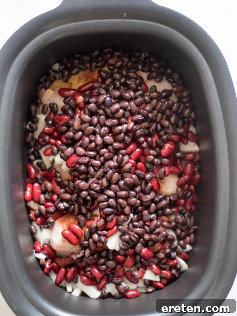 Black beans are poured into the slow cooker, joining the kidney beans, chicken, and onions to build the chili's texture and flavor.