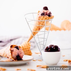 homemade black cherry ice cream in a cone drizzled with cherry juice down the side - a bowl full of cherries on the side