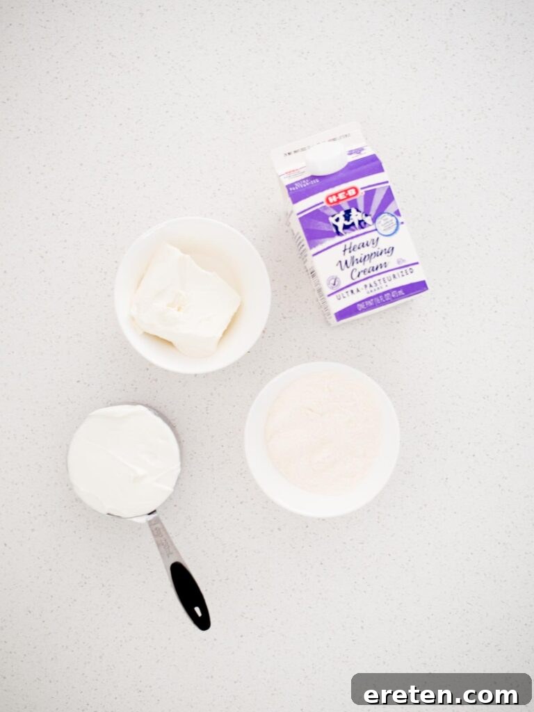 A clean, organized shot showcasing the four simple ingredients needed to make the yogurt fruit dip: a container of vanilla yogurt, a block of cream cheese, a carton of whipping cream, and a box of instant vanilla pudding mix, ready for assembly.