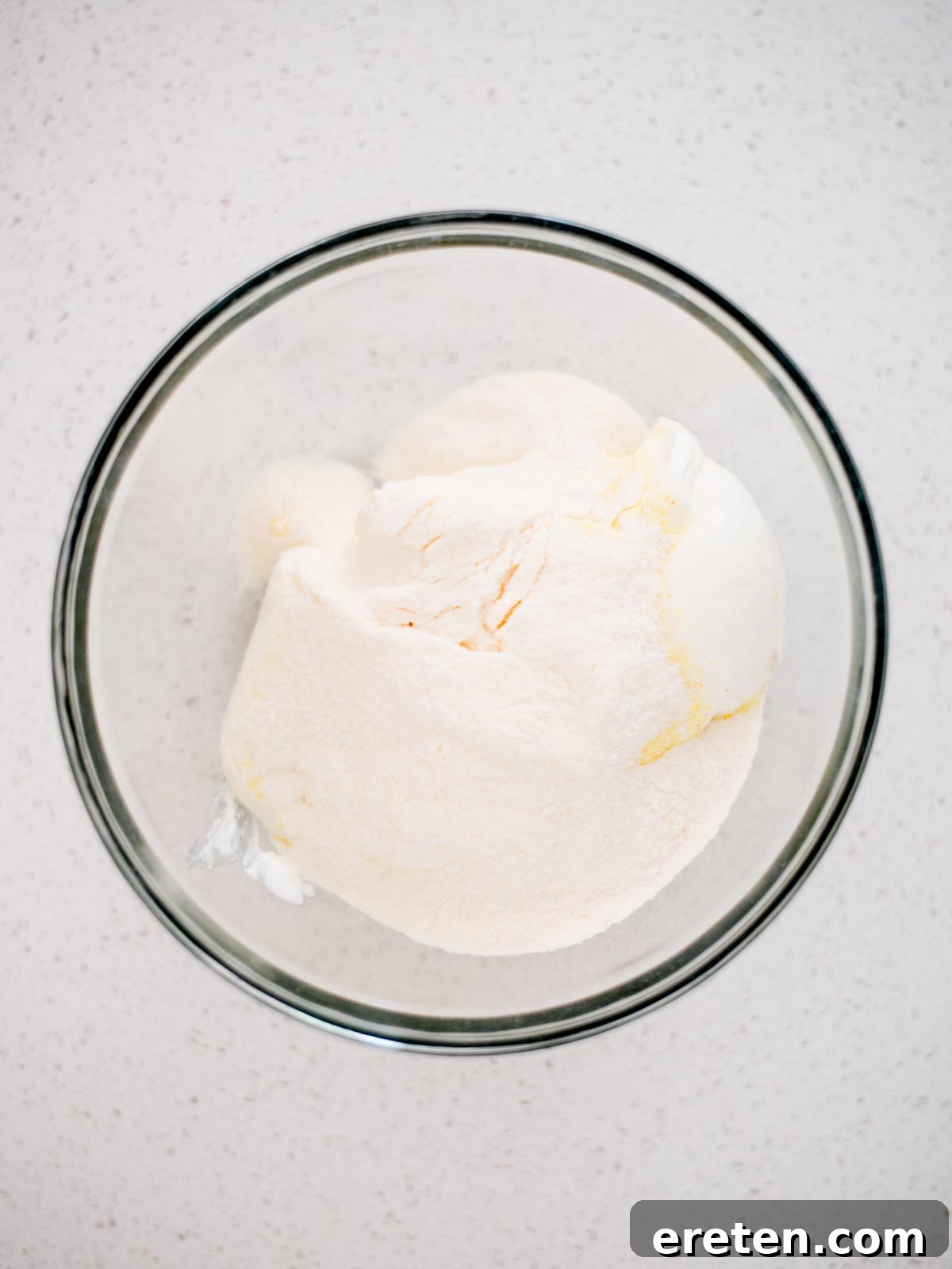 All the creamy ingredients for yogurt fruit dip, including vanilla yogurt, softened cream cheese, whipping cream, and vanilla pudding mix, are gathered in a large mixing bowl, ready to be whipped into a smooth consistency.