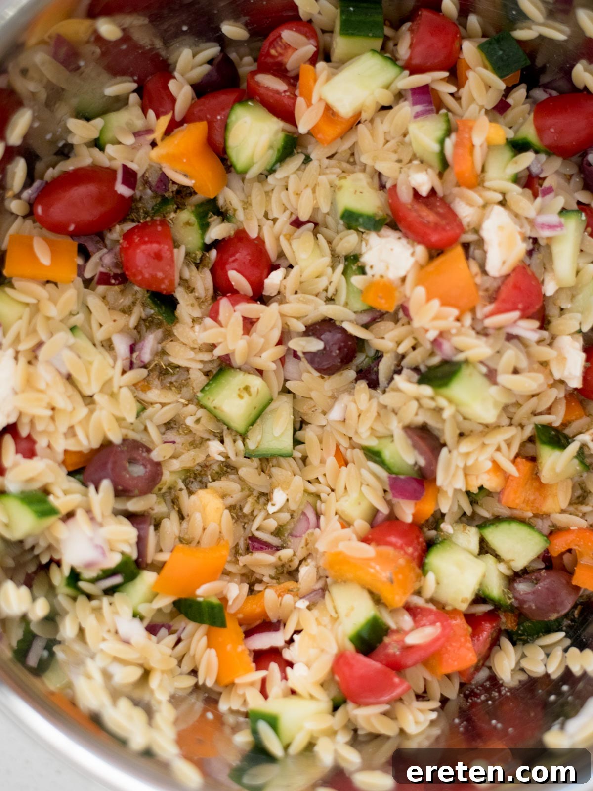 dressing added to orzo and vegetables in a mixing bowl