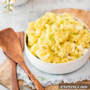 old fashioned potato salad in a white bowl topped with fresh dill