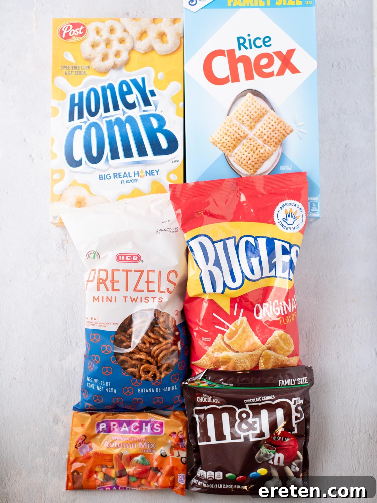 Six snack packages—Honeycomb cereal, Rice Chex, H-E-B pretzels, Bugles, Brach’s Autumn Mix candy, and M&M’s—arranged on a light surface in two rows.