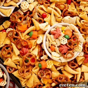 A close-up of snack mix with pretzels, Bugles, cereal pieces, candy pumpkins, candy corn, and colorful chocolate candies, with a small white bowl filled with the mix in the center.