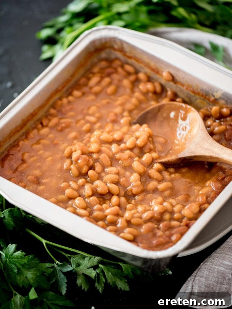 A close-up of smoked baked beans, showing their rich, savory texture, with a spoon nestled inside the dish, ready to be served.
