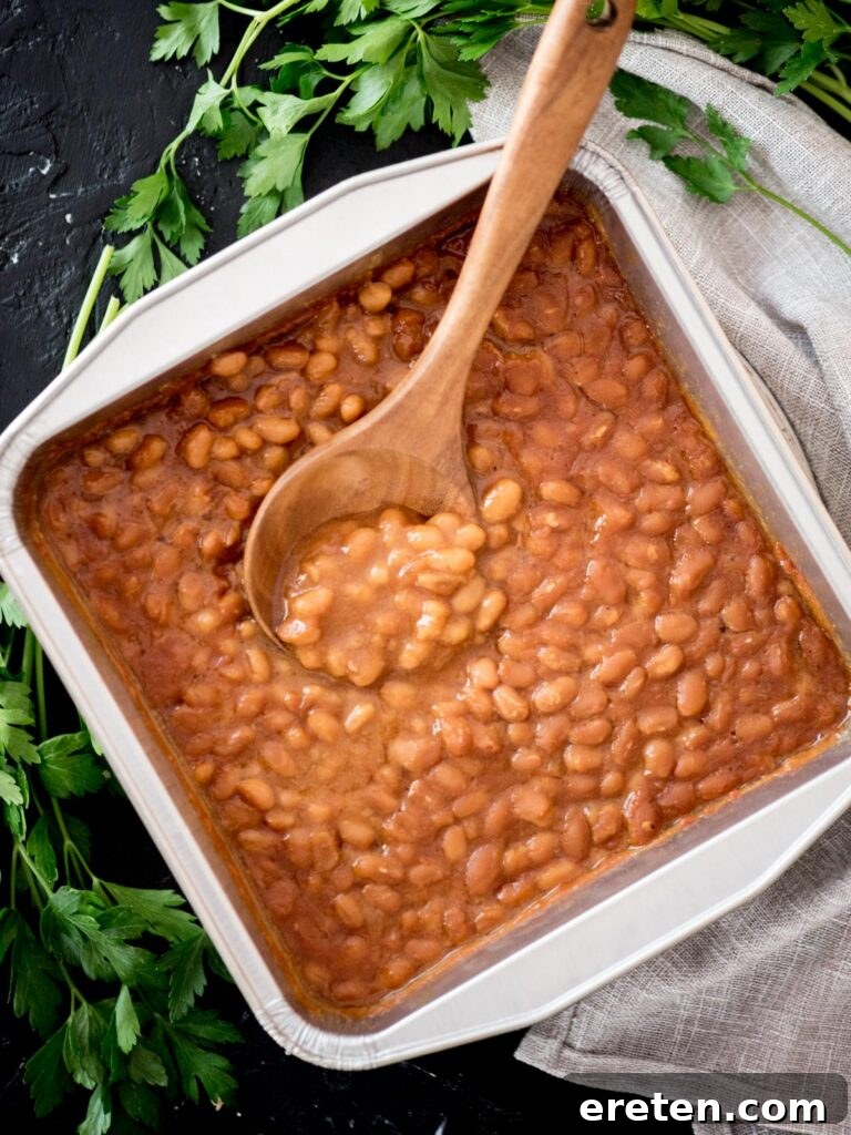 A dish of freshly smoked baked beans, bubbly and hot, with a serving spoon, presented in a rustic container.