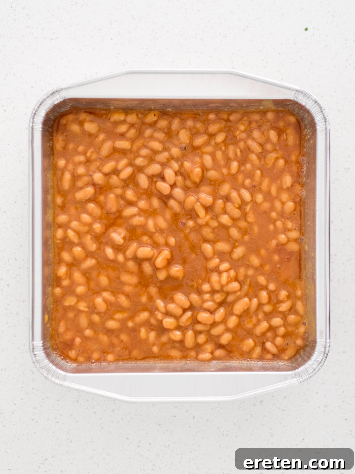 The pan of mixed baked beans positioned on the smoker grill grates, just before the smoking process begins.