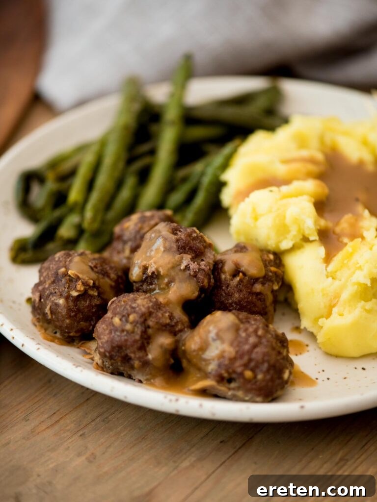 plated french onion meatballs generously covered in gravy, accompanied by a scoop of fluffy mashed potatoes and a vibrant serving of roasted green beans