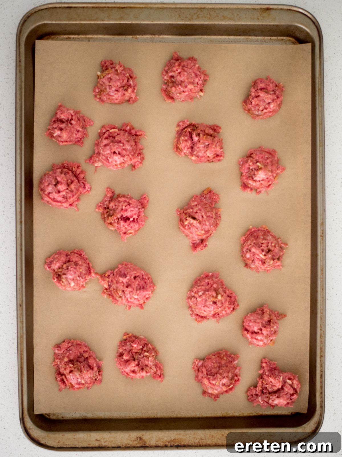 meatball mixture being scooped onto a parchment-lined baking sheet using a cookie scoop to ensure uniform size