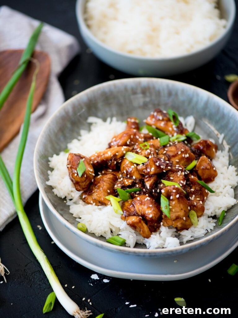 A vibrant bowl of homemade General Tso Chicken, garnished with fresh green onions, served alongside fluffy white rice, ready to be enjoyed.