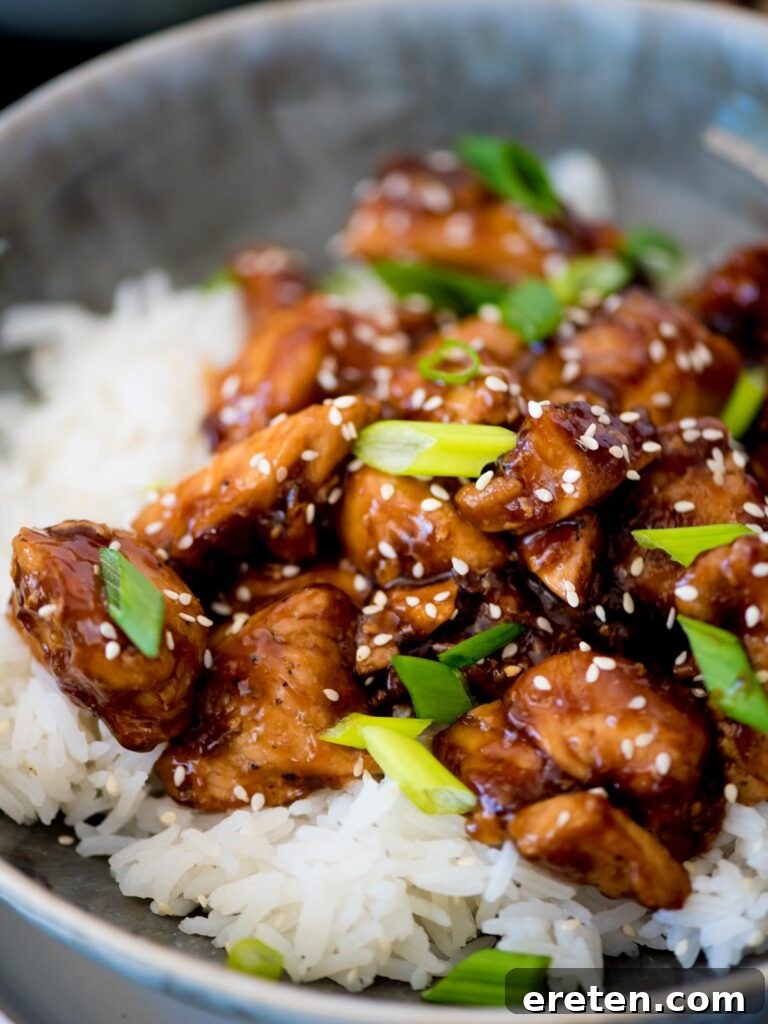 A beautifully presented bowl of General Tso chicken and white rice, artfully garnished with vibrant sliced green onions.