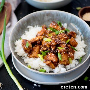 General Tso chicken and rice in a bowl garnished with sliced green onions.