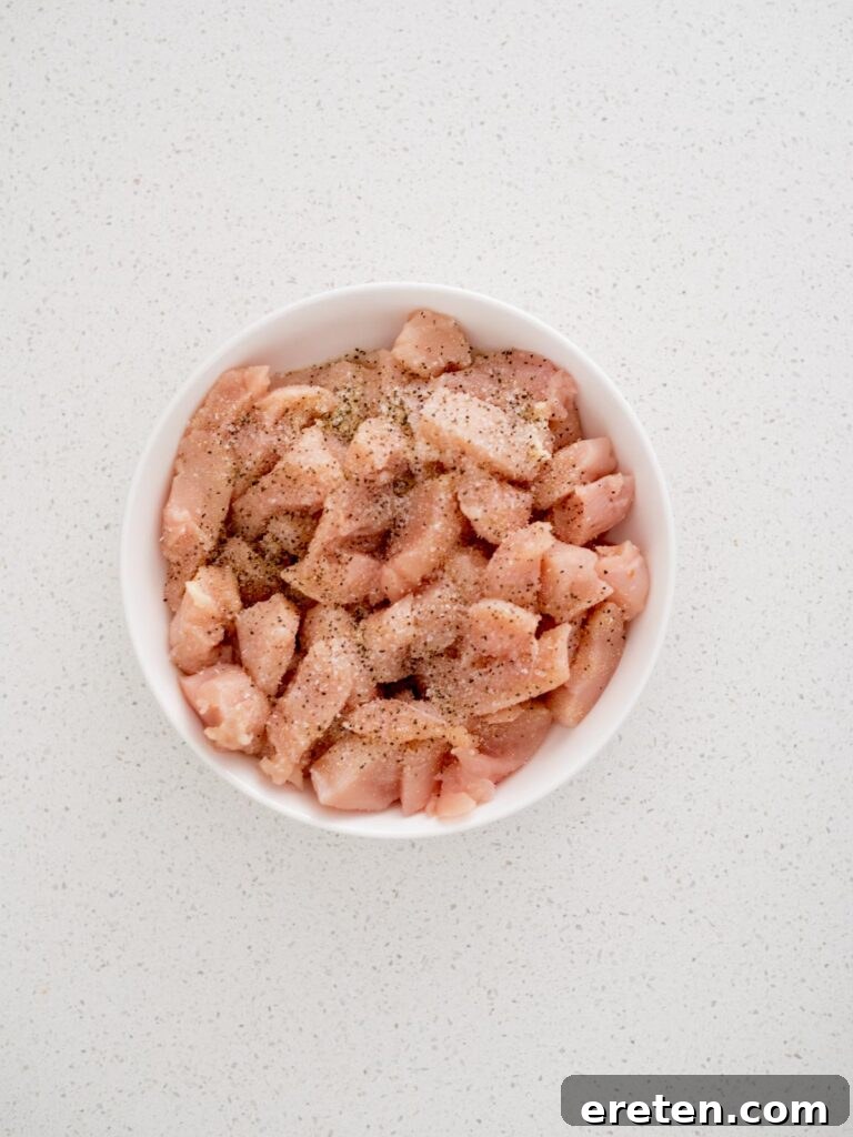 Seasoning sprinkled over raw chicken chunks in a bowl, preparing them for cooking.
