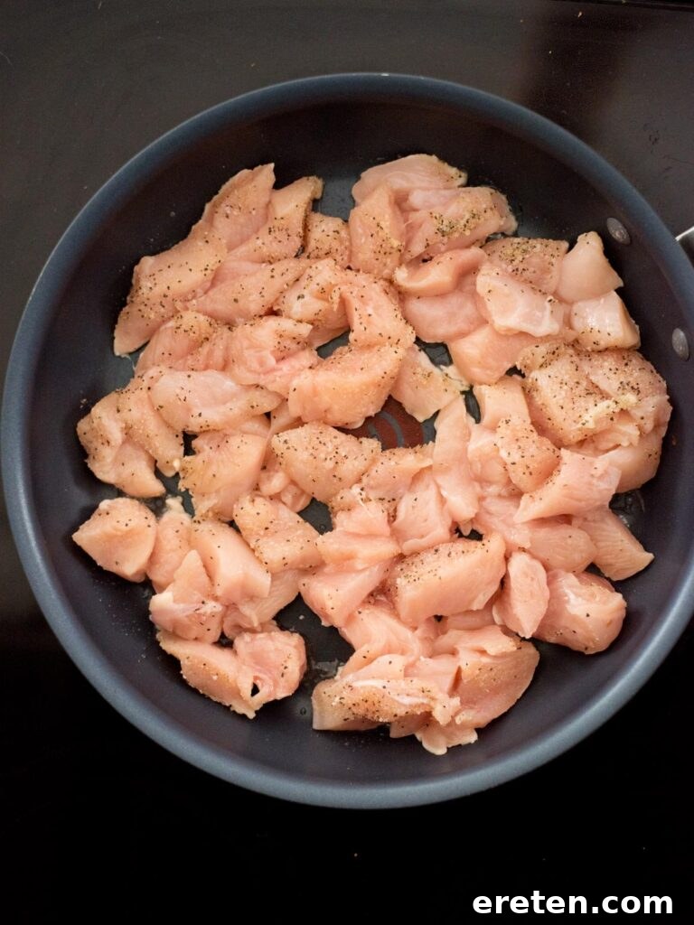 Raw chicken cut into chunks and added to a hot frying pan, beginning the pan-frying process.