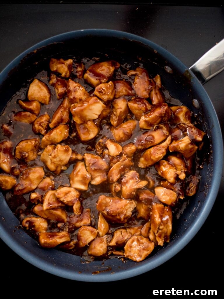 A frying pan showing chicken chunks generously coated in a glossy, thickened General Tso sauce.