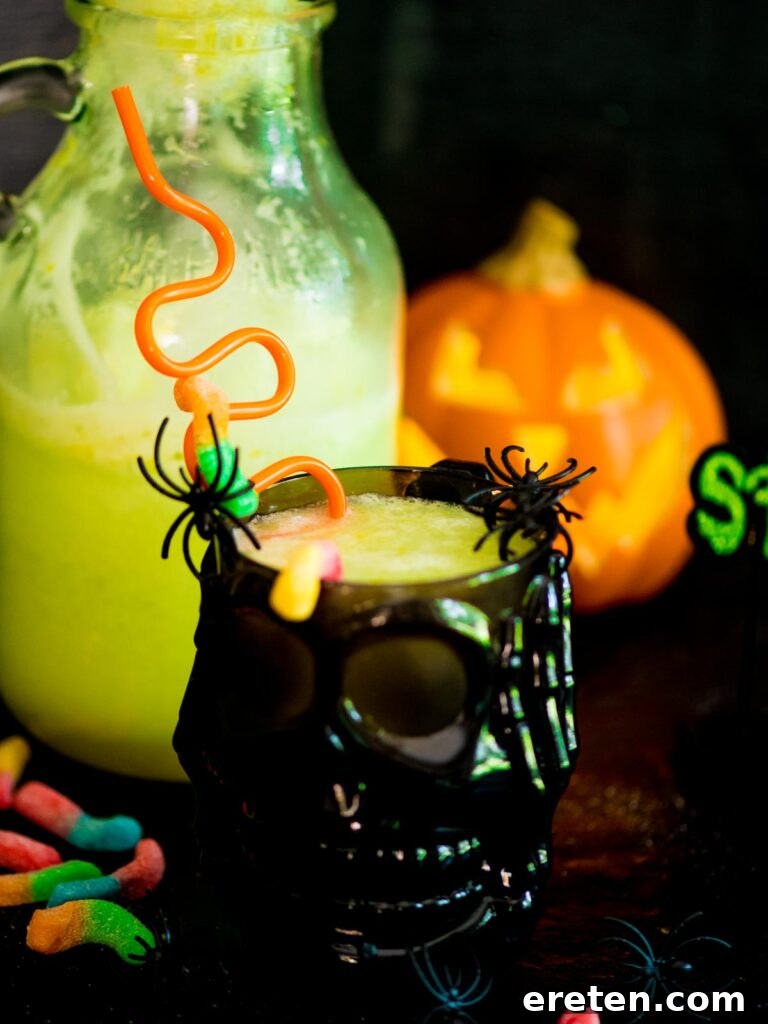 Vibrant green Bug Juice drink in a skull-shaped cup, garnished with plastic spiders and gummy worms, perfect for a spooky Halloween party.
