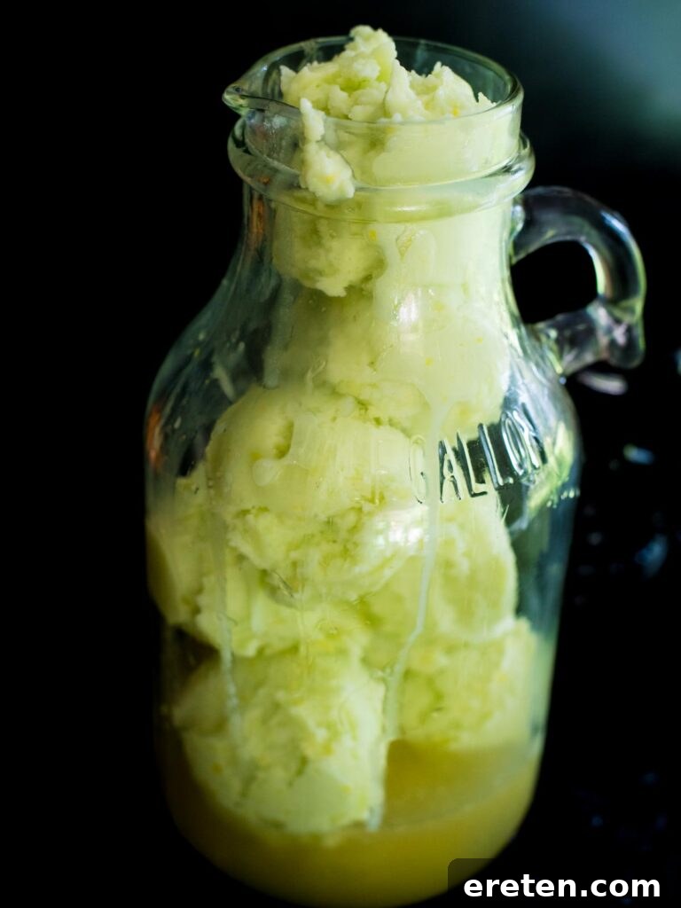 Scoops of lime sherbet being gently added to the green limeade and Sprite mixture in a pitcher, creating a frothy layer.