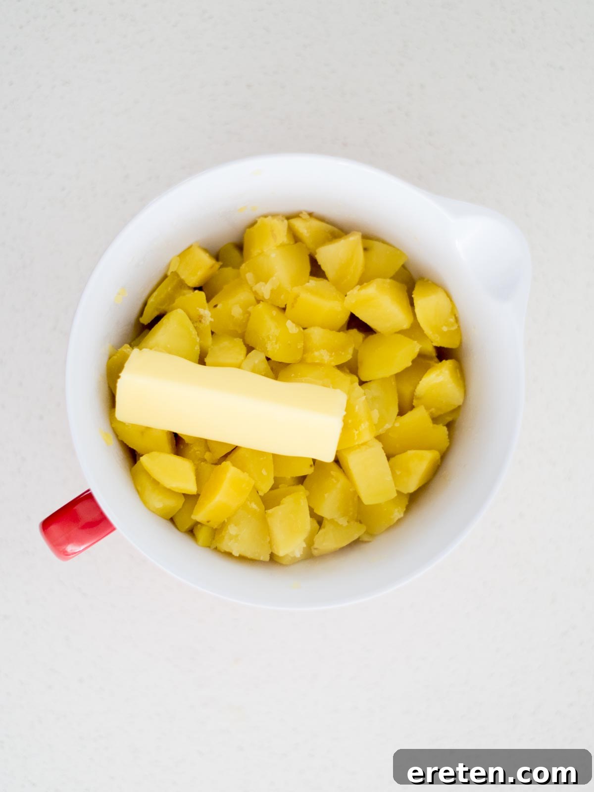 Mixing bowl with cut up cooked potatoes and a stick of butter added to the top.