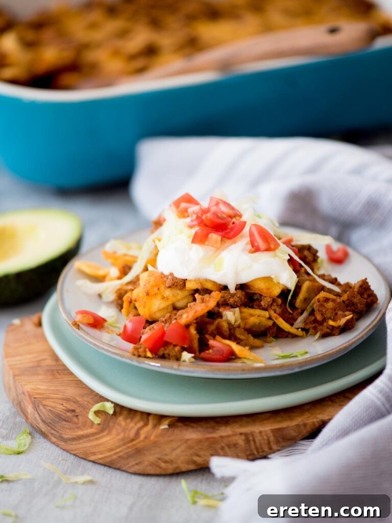A serving of Walking Taco Casserole topped with sour cream and diced tomatoes on a plate, ready to be enjoyed.