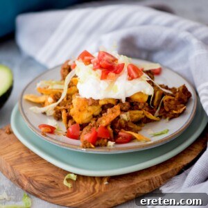 A small plate with a serving of walking taco casserole on it and garnished with sour cream and diced tomatoes.