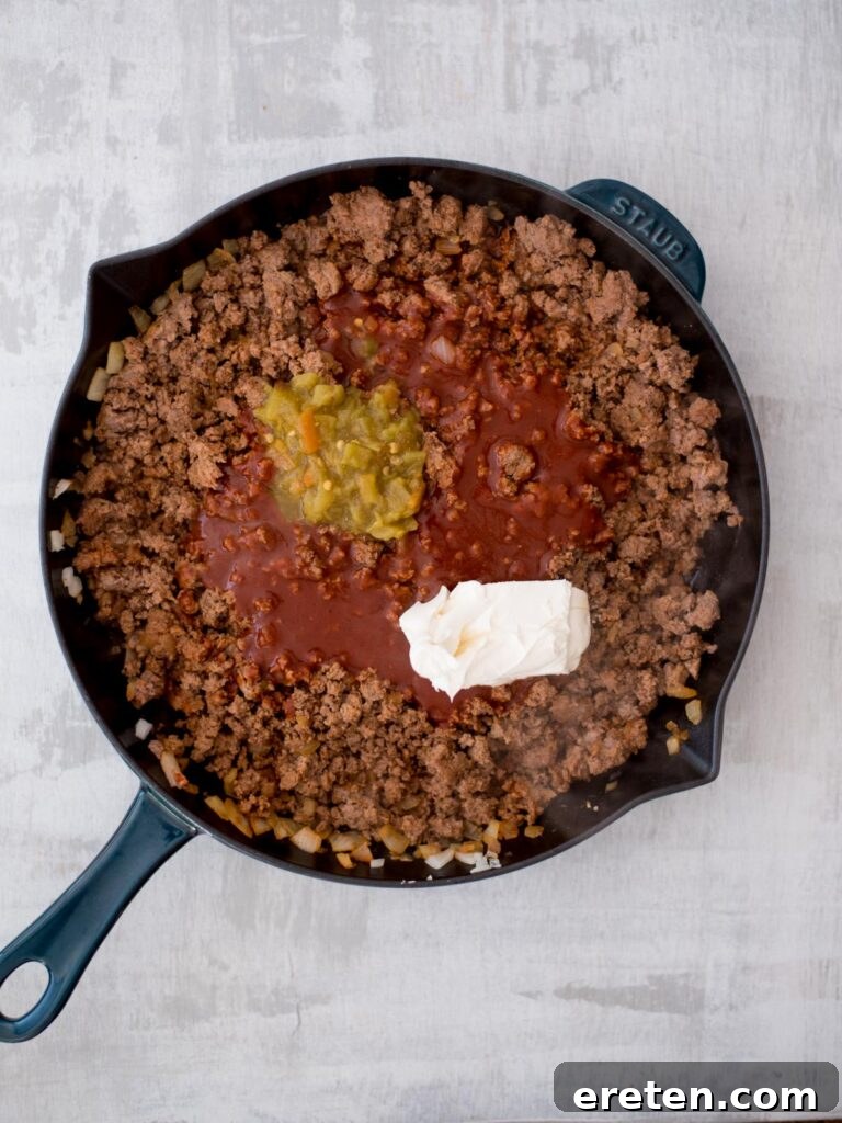 Cooked and browned ground beef in a cast iron pan, with seasonings being stirred in to infuse the meat with flavor.