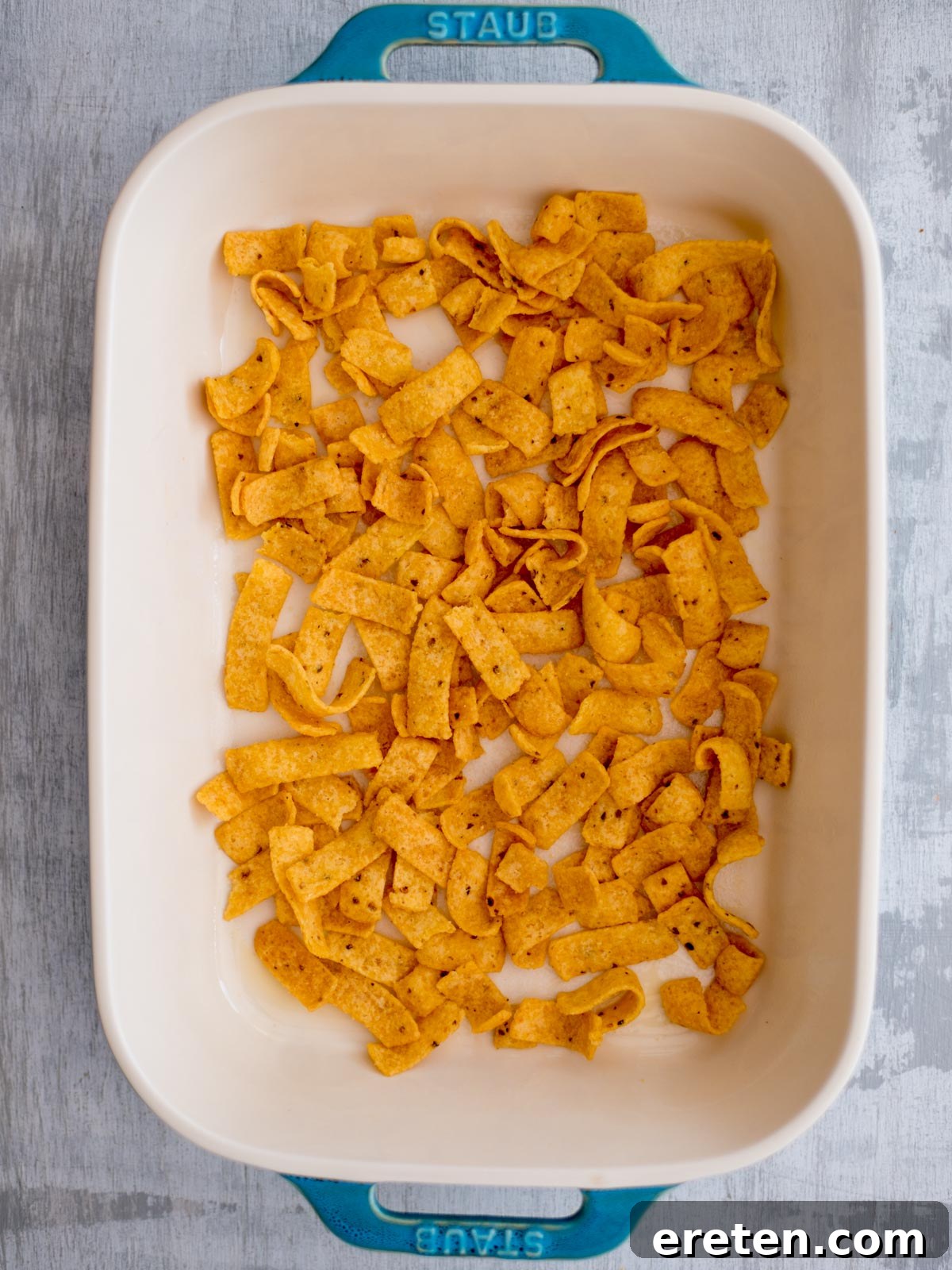 The bottom of a casserole dish covered with a uniform layer of Frito corn chips, ready for the next delicious layer.
