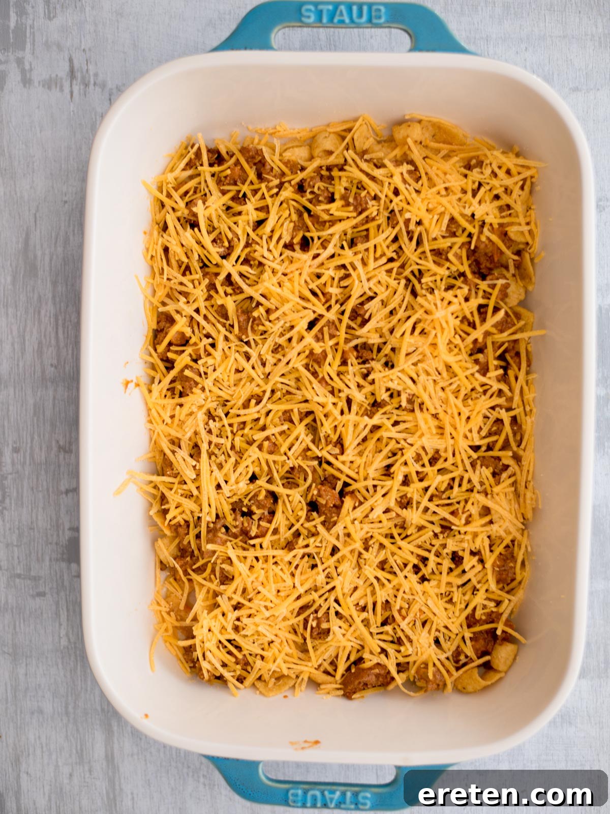 A generous sprinkling of shredded cheese covers the seasoned ground beef and Frito layers, forming a delicious, melty top.