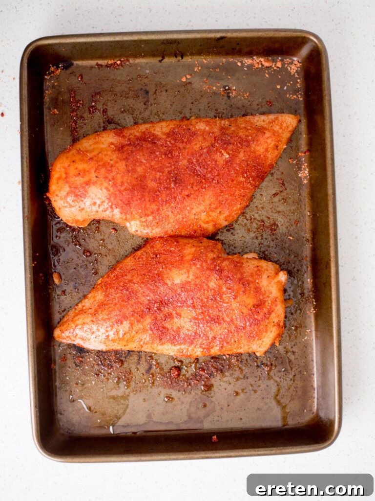 Flavorful Smoked Chicken Breast from Your Pellet Grill 4 Two uncooked chicken breasts, generously seasoned with dry rub, resting on a baking sheet.