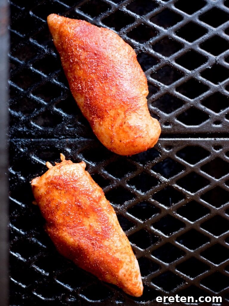 Flavorful Smoked Chicken Breast from Your Pellet Grill 5 Two seasoned chicken breasts smoking on the grates of a pellet grill, with visible smoke.