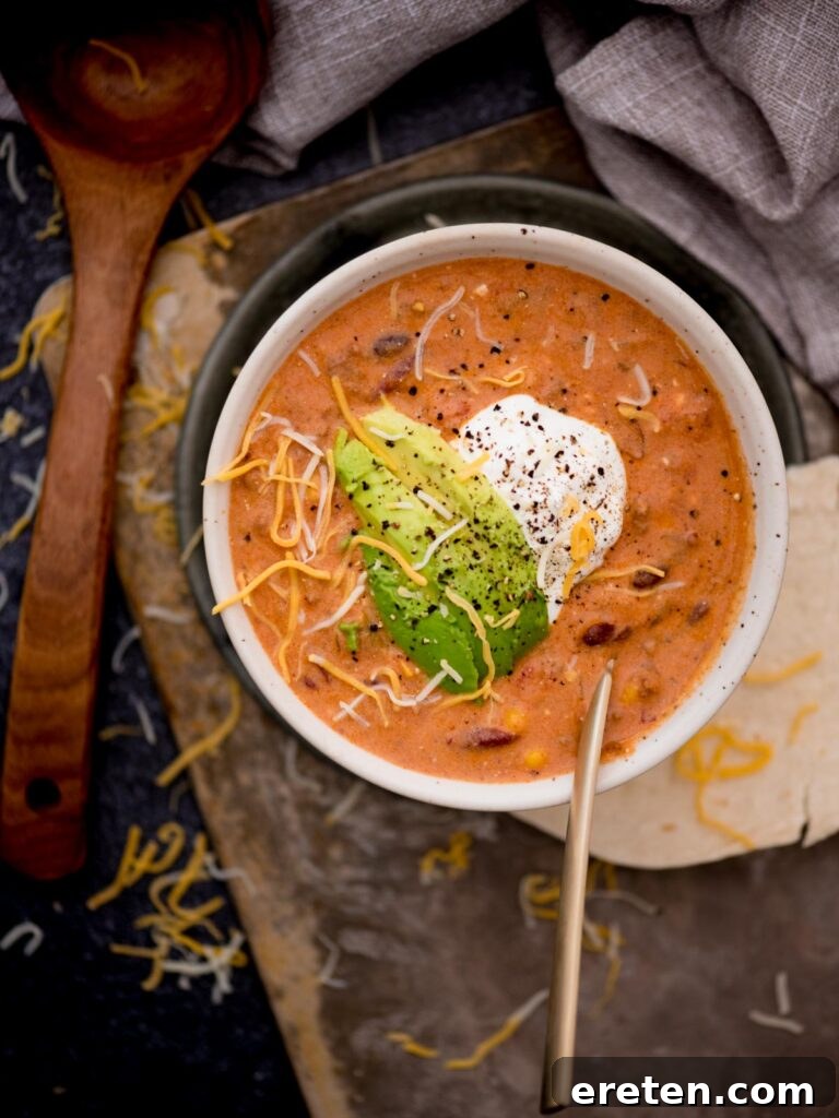 A steaming bowl of creamy taco soup, garnished with a generous dollop of sour cream and fresh avocado slices, ready to be enjoyed.
