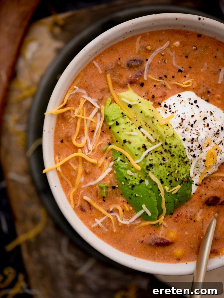 A close-up view of a bowl of creamy taco soup, artfully topped with fresh avocado and sour cream, showcasing its rich texture.